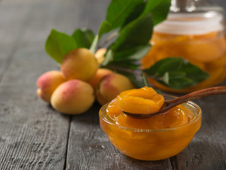 A jar of apricot jam and fresh berries on a wooden table.