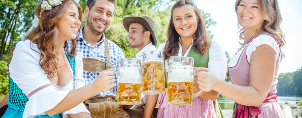 Five friends, men and women, having fun on Bavarian RIver and clinking glasses with beer