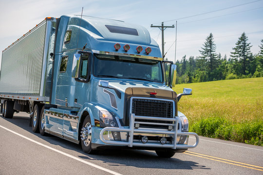 Big rig blue semi truck with grille guard transporting cargo in grooved semi trailer driving on the summer road