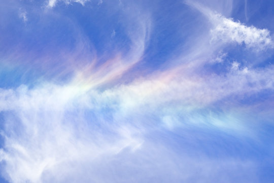 Cloud iridescence or irisation visible on the surface of white cirrus clouds; blue sky background