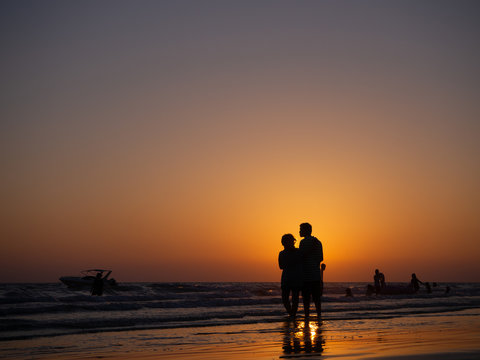 silhouette couple in love walking on beach with orange evening sky background, honeymoon as concept.