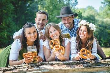 Freunde in bayerischen Tracht feiern an der Isar und trinken Bier. Oktoberfest München