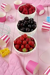 Berry baking. Raspberry, cherry, strawberry muffins.Summer berries in round cups set, pink oven gloves, pink striped and speckled cupcakes on a  wooden background.Healthy Diet Sweets