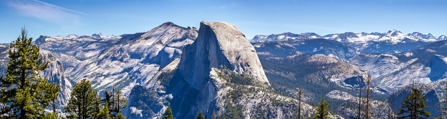 Panoramic view of the majestic Half Dome and the surrounding wilderness area with mountain peaks and ridges still covered by snow; Yosemite National Park, Sierra Nevada mountains, California