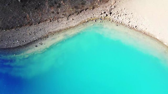 Krafla Viti crater is in Myvatn, filled with turquoise water and is surrounded by a geothermal area and colorful mountains. Drone shot moving forward panning up revealing mountains beyond rim.