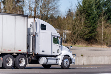 White big rig semi truck transporting commercial cargo in dry van semi trailer running on divided road