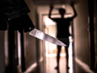 Hand with knife following young terrified in the apartment. man Bandit is holding a knife in hand,...