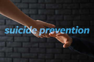 Woman giving hand to depressed man against dark background. Suicide prevention concept