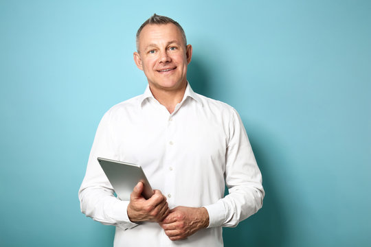 Handsome middle-aged man with tablet PC on color background