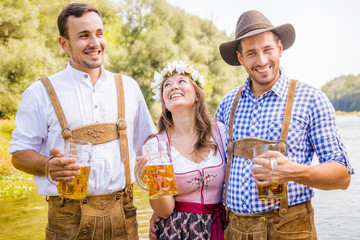 Freunde in bayerischen Tracht feiern an der Isar und trinken Bier. Oktoberfest München