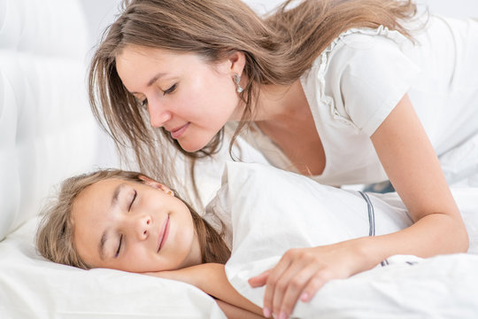 Young mother wakes up a happy daughter with a kiss