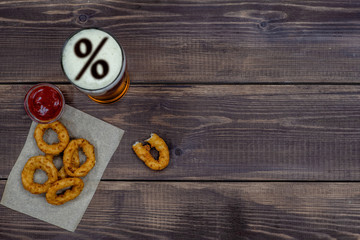 Snacks and beer with percent sign on a beer foam on dark wooden background. Top view. Empty space for text