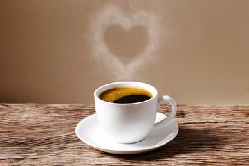 Heart of steam hovering over a red coffee cup of coffee on wooden table with cream wall background.