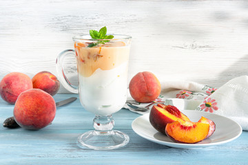 Glass of yogurt with slices of sweet ripe juicy fruit, peaches with green leaves in a basket on white background
