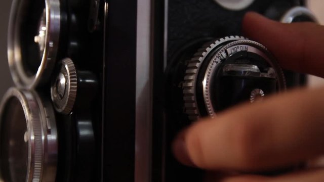 girl's hand twists the focus wheel of a vintage medium format camera.