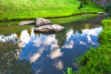 large stones in the river with the reflection of trees