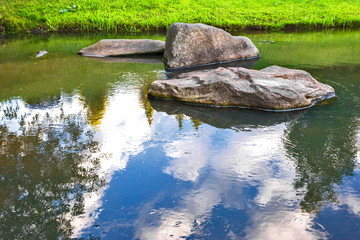 large stones in the river with the reflection of trees
