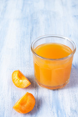 Ripe apricots and glass of apricot juice on blue rustic background with copy space. Selective focus. Eco food concept. Fresh summer drinks. Detox. Non alcoholic. Vertical