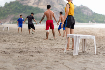 Selected focus group of friends playing soccer on the beach in summertime.