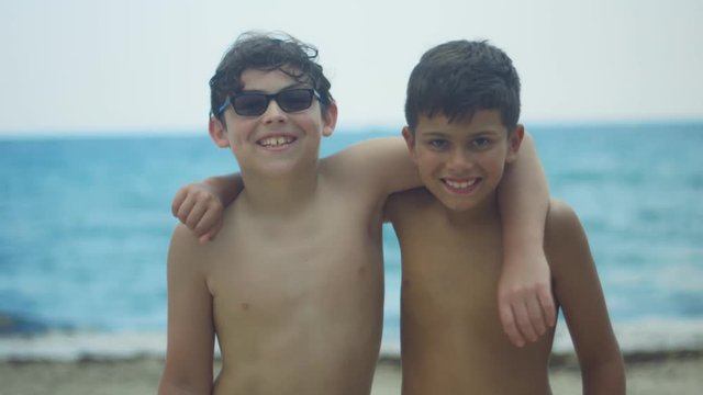 Slow motion of two kids hugging and smiling at camera at the beach