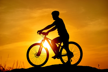 Silhouette man and bike relaxing on blurry sunrise sky background.