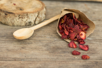 Dry strawberry chips wrapped in paper wooden background