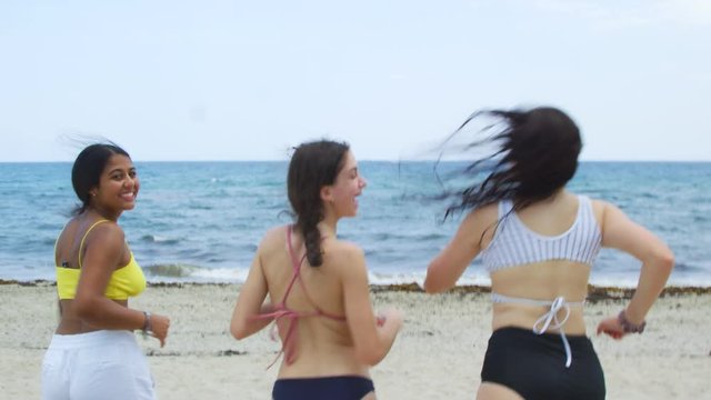 Slow motion of teenagers at the beach running towards the ocean 
