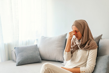 Sinus pain, sinus pressure, sinusitis. Sad Muslim woman holding her nose and head because sinus...