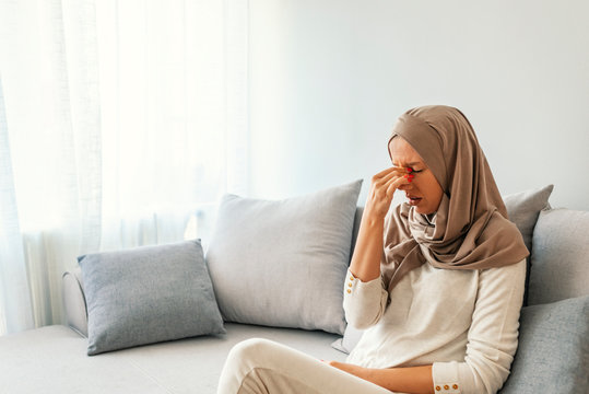 Sinus pain, sinus pressure, sinusitis. Sad Muslim woman holding her nose and head because sinus pain. Sinus ache causing very paintful headache. Unhealthy woman in pain. Sharp strong sore