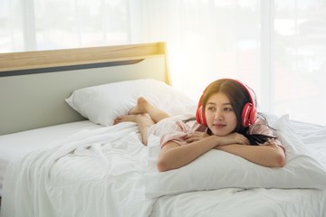 Portait of smiling lady in pink pajama wake up listening to music with headphone light on the bed