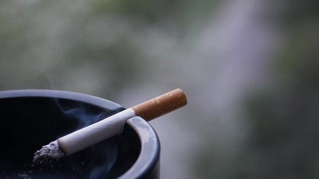 Cigarette burning in ashtray, nicotine addiction, cigarette with smoke rest on the black ashtray.