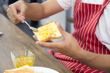 Man in red apron spreading sweet orange peel jam on toast with sun icon over table