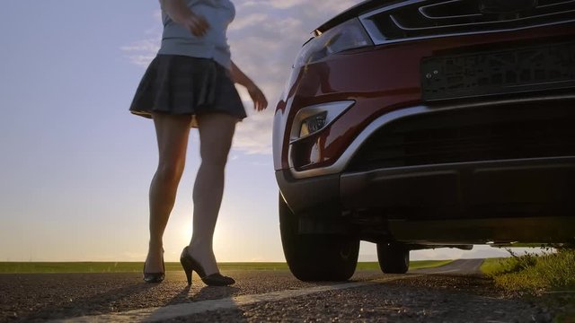 woman in short skirt leaning over hood of car at sunset.