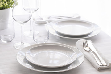 Table setting white and grey colour. Empty glasses and plates set with napkin and cutlery. Restaurant interior background...