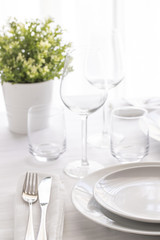 Table setting white and grey colour. Empty glasses and plates set with napkin and cutlery. Restaurant interior background...