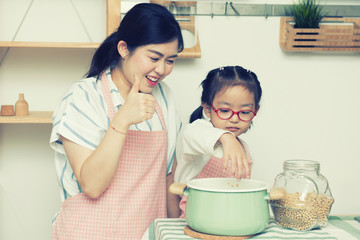 Asian woman mom with daugther in kitchen,little girl play with peanut and mom thrump up with happy...