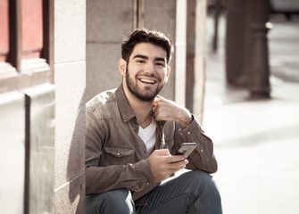 Young attractive happy stylish man on smart phone social network app in european city outdoors