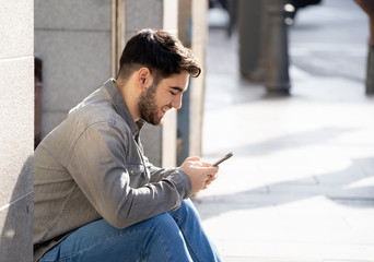 Young attractive happy stylish man on smart phone social network app in european city outdoors