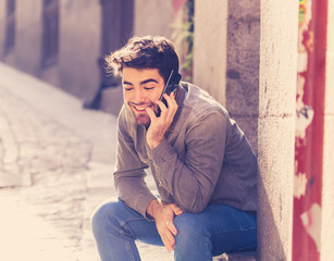 Obraz premium Young attractive happy man talking on smart phone in european city