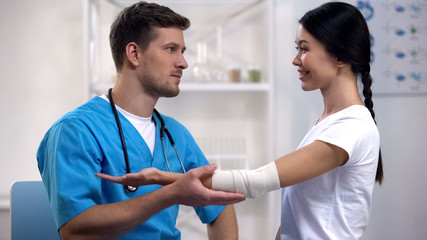 Traumatologist fixing elbow elastic wrap of female patient, flirting and smiling