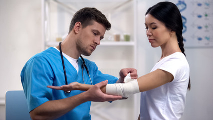 Attentive therapist fixing elbow elastic warp female patient after injury health