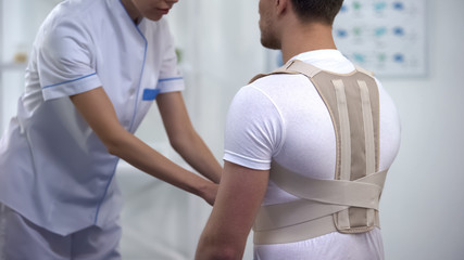 Orthopedist applying posture control shoulder brace male patient, healthcare - obrazy, fototapety, plakaty