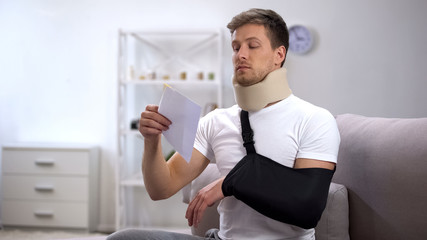 Injured man in foam cervical collar and arm sling trying to open envelope, bill