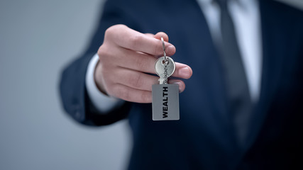 Wealth word on keychain in businessman hand, key tips to successful rich life