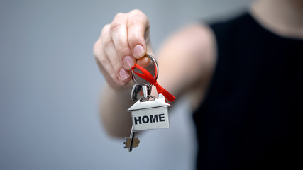 Woman holding keychain with word Home, long-awaited house purchase, closeup