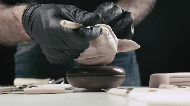 Artist models a plasticine puppet head's eye bulb with a needle tool