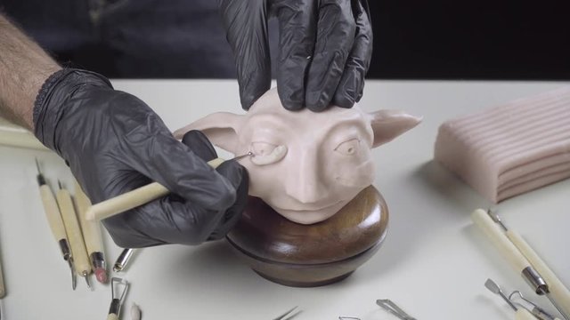 Artist models a plasticine puppet head's eye with a needle tool 4K