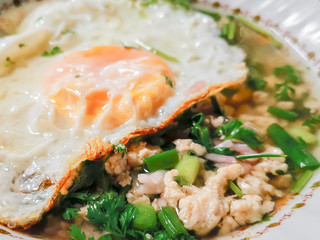 Close up Hot Thai boiled rice soup with minced chicken, fried egg and green scallion chop in bowl.