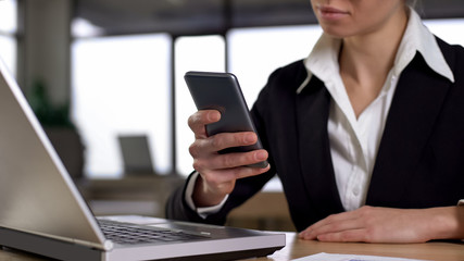 Female using cellphone in office, concept of mobile and laptop synchronization