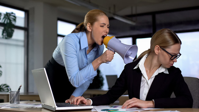 Female boss screaming with megaphone at colleague, authoritarian leadership